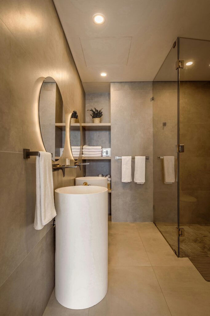 Elegant minimalist bathroom featuring a round lit mirror and sleek fixtures in neutral tones.